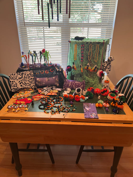 Wide view of Halloween grab bag examples on a green-topped table, including beaded jewelry, pouches, pencils, small pumpkins, and a hanging ghost.