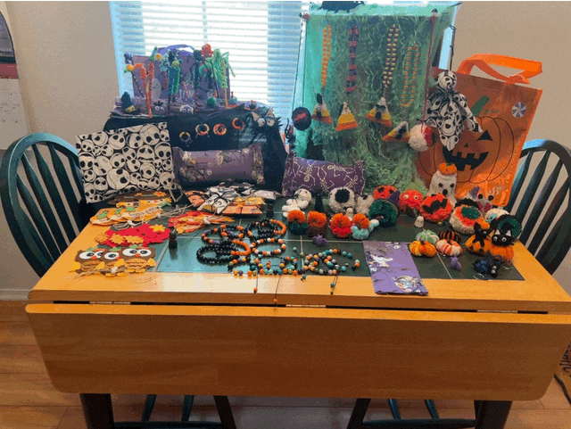 Close-up of Halloween grab bag examples on a green-topped table, including beaded jewelry, a pouch, earrings, and small pumpkins.