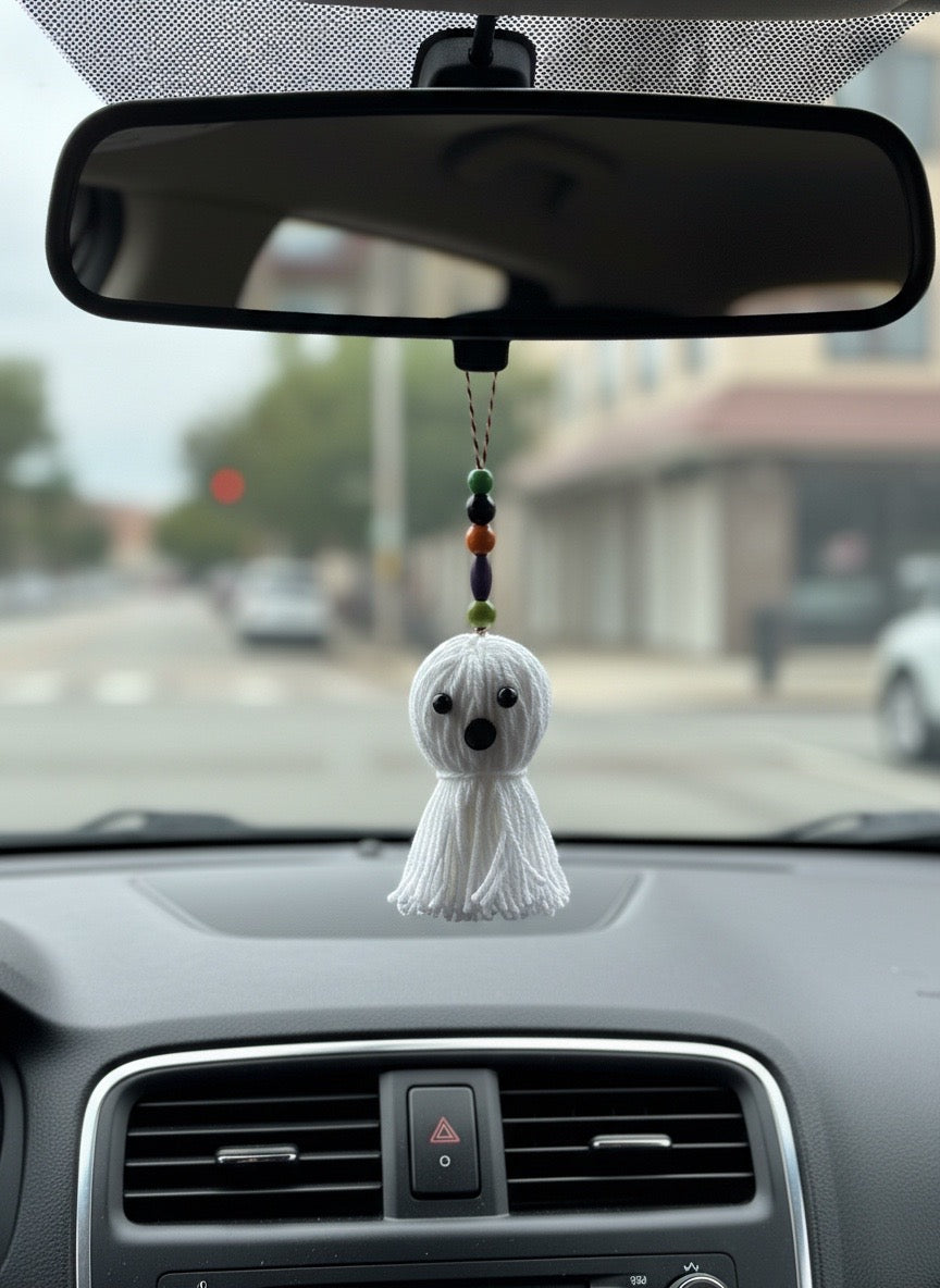 A white yarn ghost door knob hanger with colorful beads hanging from a car's rearview mirror.