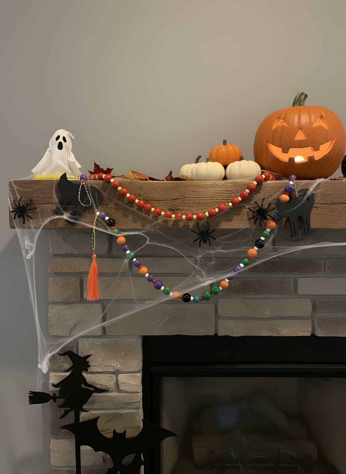 Handmade Halloween beaded garland draped along a wood mantel with a carved jack-o'-lantern, white pumpkins, a ghost and cobwebs, shown with a second garland.