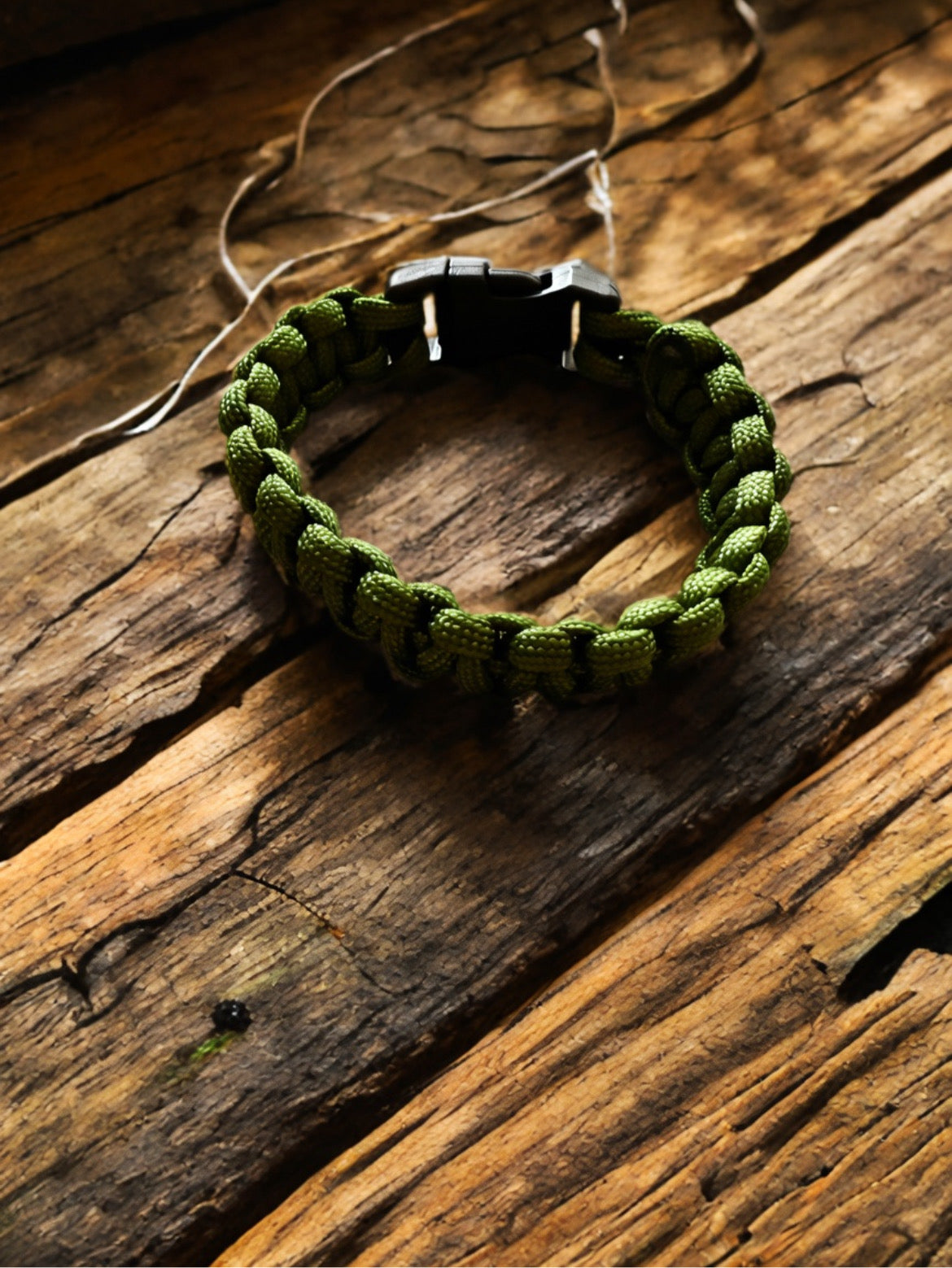 Army green paracord survival bracelet resting on a rustic wood background.